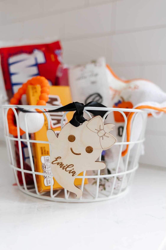 Wooden ghost name tag with floral engraving tied to a Halloween treat basket.
