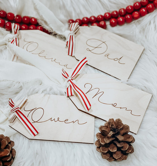 Engraved rectangular wooden stocking tags reading Olivia, Dad, Mom and Owen with striped ribbon ties.