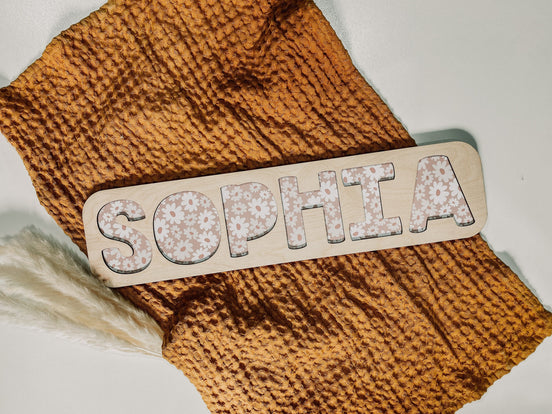Personalized SOPHIA name puzzle with pink floral-patterned letters on a pale wooden board.