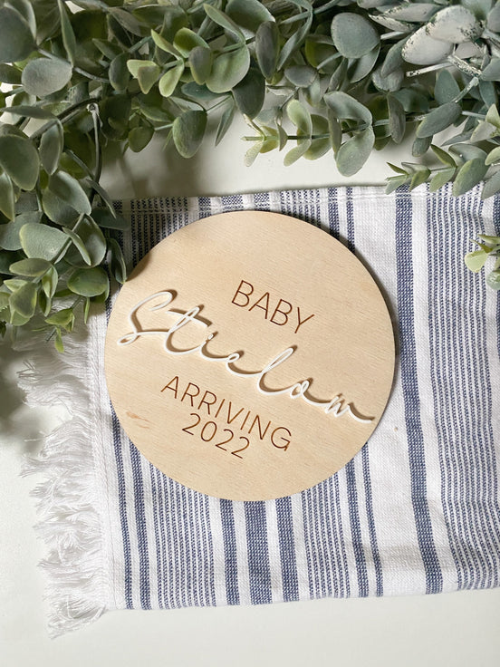 Baby Edwards pregnancy announcement disc with raised script and an engraved April 2022 arrival date.