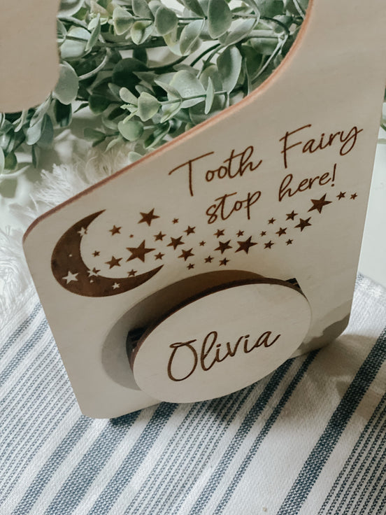 Angled close-up of the Tooth Fairy Stop Here engraving and Olivia compartment on a wooden hanger.