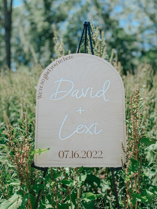 David and Lexi wedding welcome sign on a black easel among garden greenery.
