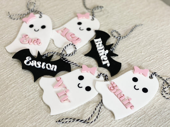 Assorted ghost and bat name tags with pink bows, flowers and black-and-white cords.