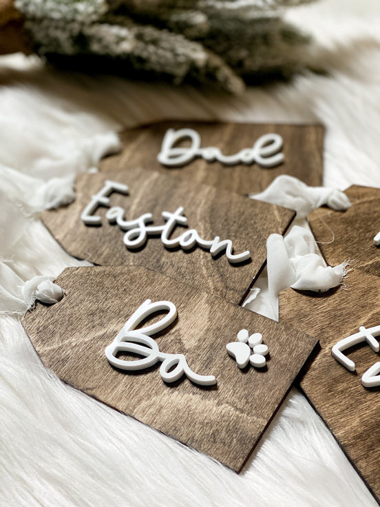 Close-up of raised white names and a paw-print detail on dark wooden stocking tags.