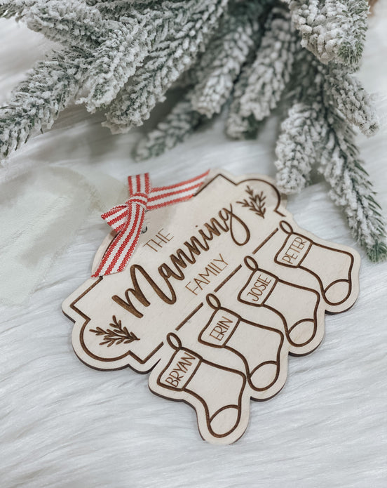 Personalized wooden family ornament with four engraved stocking names and a red-and-white bow.