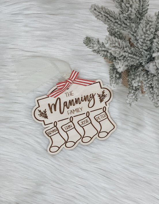 Full view of the family stocking ornament on a white surface beside frosted greenery.