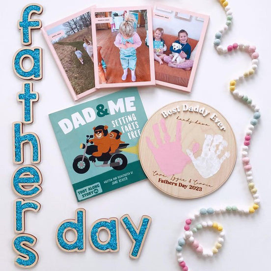 Father's Day flat lay with a handprint plaque, family photos, a Dad and Me book and decorative lettering.