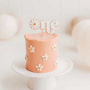 White One cake topper with a daisy-shaped O on a peach cake decorated with daisies.
