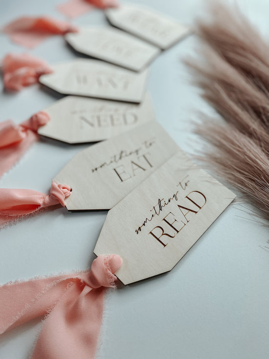 Close-up of engraved gift-category tags with pink ribbons, including Read, Eat and Need.