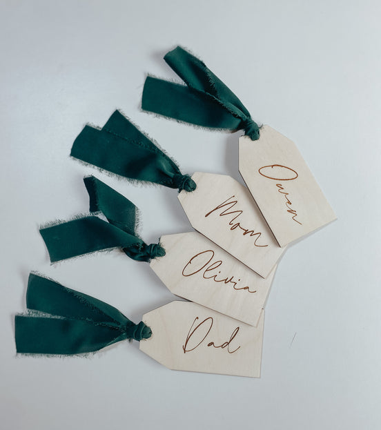 Four engraved rectangular wooden family stocking tags with dark green ribbon loops on a pale surface.
