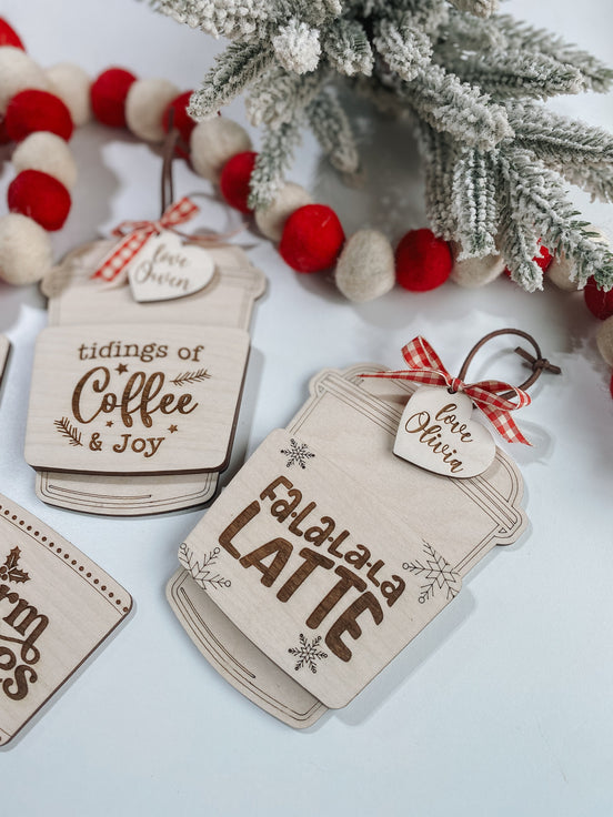Tidings of Coffee and Joy and Falalala Latte gift-card ornaments beside frosted greenery.