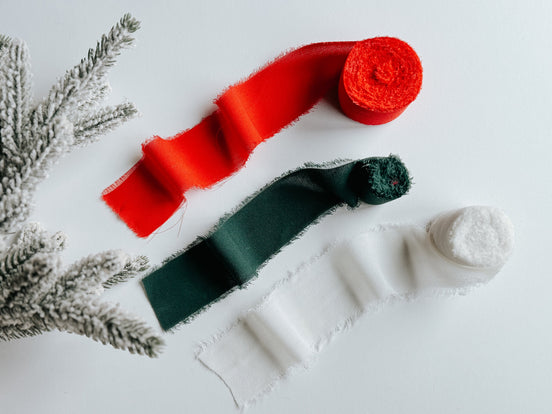 Red, dark green and white ribbon rolls displayed beside an evergreen branch.