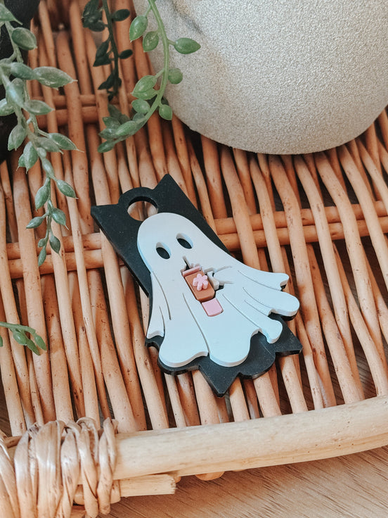 Ghost-with-drink tumbler topper on a black outline base lying on a wicker surface.