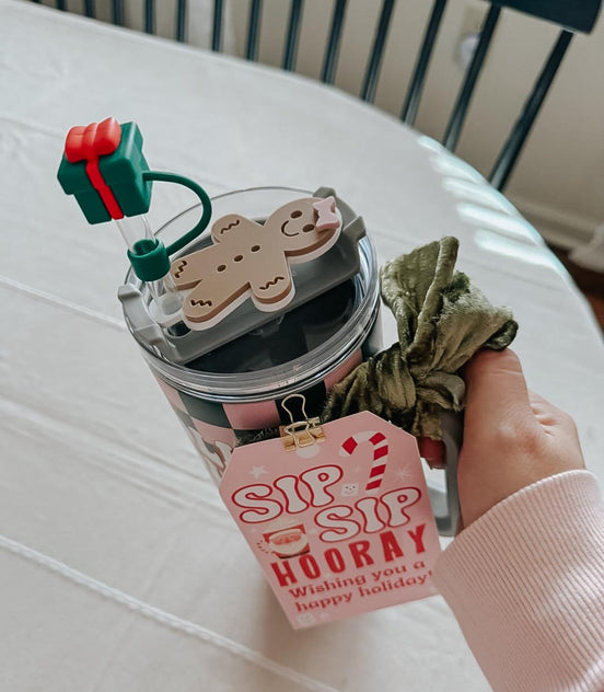 Hand holding a decorated holiday tumbler with a gingerbread topper, bow and gift tag.