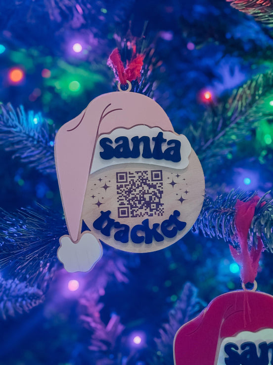 Wooden Santa Tracker QR ornament with raised blue lettering and a Santa hat on a colorful Christmas tree.