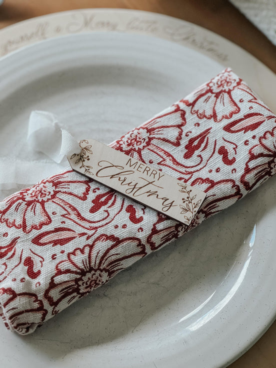 Engraved Merry Christmas wooden tag tied around a red-and-white patterned napkin.