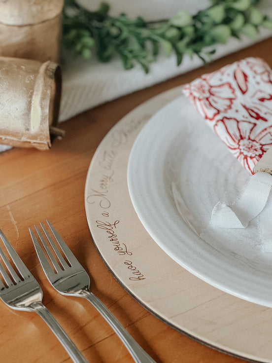 Close-up of the engraved holiday message around a wooden plate charger's edge.