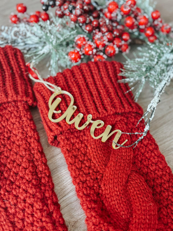 Gold Owen script stocking name tag on a red knitted stocking beside frosted greenery and red berries.