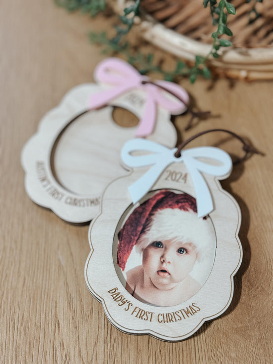 Close-up of layered baby photo ornaments with blue and pink bows and engraved Christmas details.
