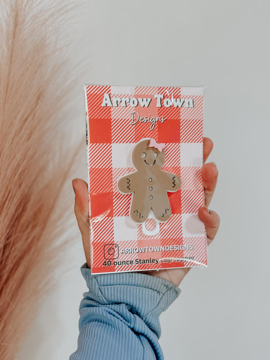 Hand holding a gingerbread tumbler topper mounted on an Arrow Town Designs packaging card.
