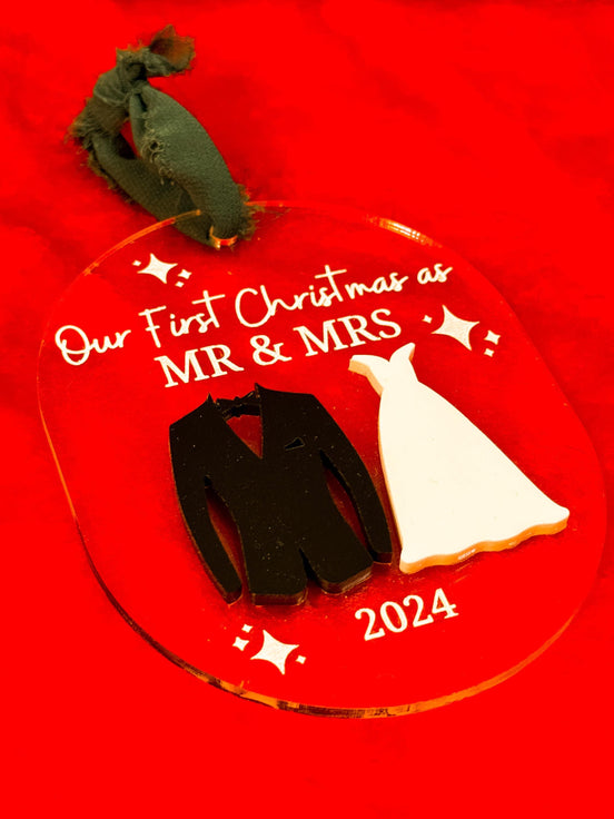 Close-up of a clear Mr and Mrs first-Christmas ornament with raised wedding outfit silhouettes and a 2024 date.