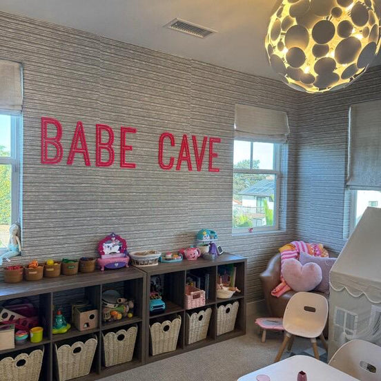 Pink BABE CAVE lettering above storage shelves in a children's playroom.