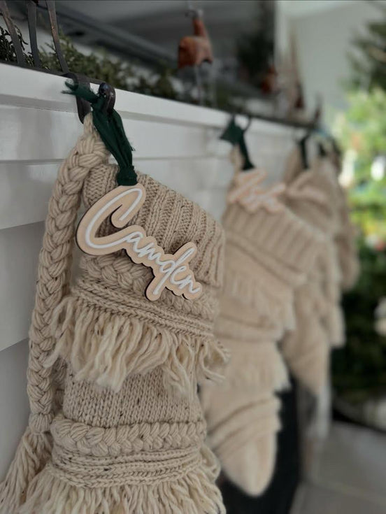 Personalized layered wooden name tag on a cream macrame stocking hanging from a mantel.