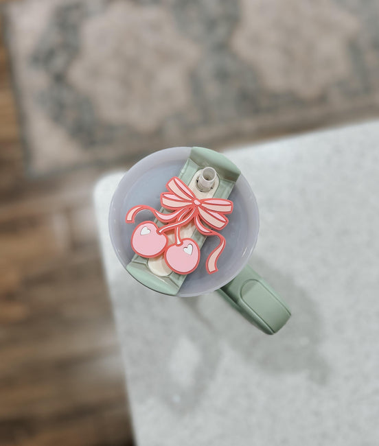 Pink cherry-and-bow tumbler topper fitted around the straw on a green handled cup.