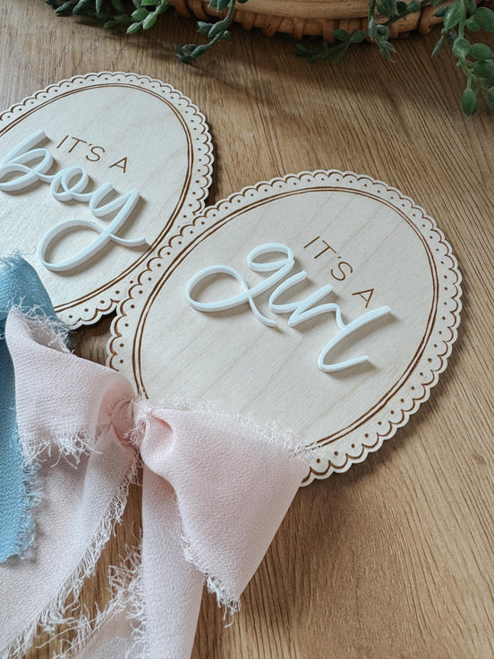 Oval It's a Boy and It's a Girl announcement plaques with lace-like borders and colored ribbons.
