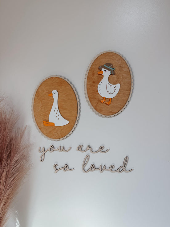 Oval wooden goose and duck wall plaques above You Are So Loved script lettering.