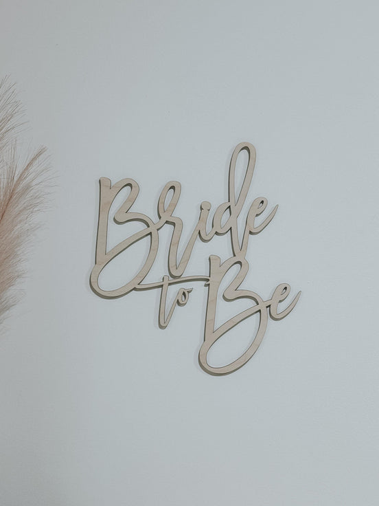 Natural wood Bride to Be script sign against a pale wall.