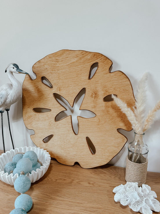Angled close-up of a wooden sand dollar beside coastal ornaments on a dresser.