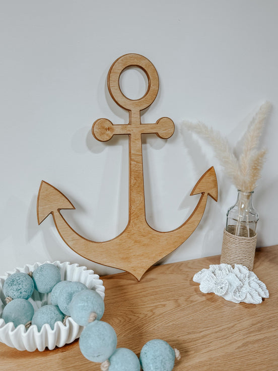 Angled view of a natural wooden anchor beside blue decorative beads, white coral and dried grasses.