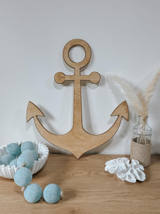 Large wooden anchor wall decoration above a dresser with blue felt garland and coastal accessories.