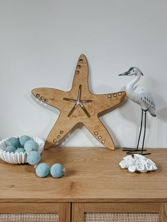 Wooden starfish wall decoration beside a seabird figure, blue felt garland and white coral.