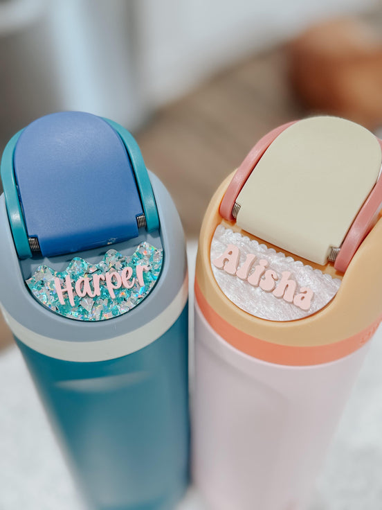 Blue and pink water bottles with personalized Harper and Alisha acrylic name plates around the lids.