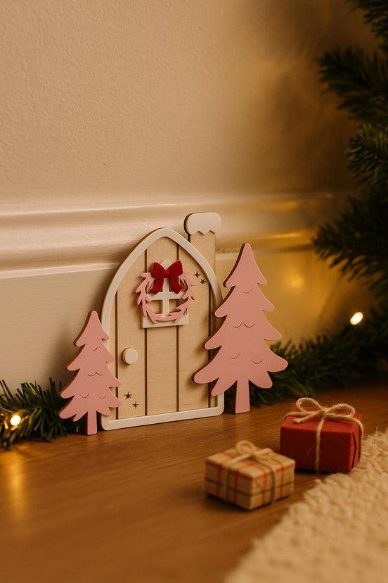 Pink-tree elf door displayed beside a baseboard with miniature gifts and holiday lights.