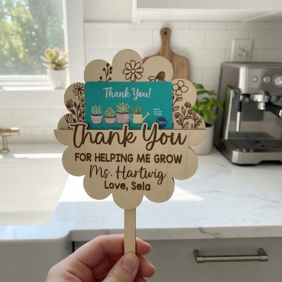 Hand holding a personalized Thank You for Helping Me Grow plant stake with a gift card inserted.
