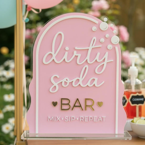Pink arched Dirty Soda Bar sign with white script, gold lettering and raised bubble details.