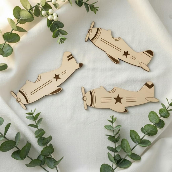 Three vintage-style wooden airplane cutouts with engraved stars and flight details arranged among eucalyptus.