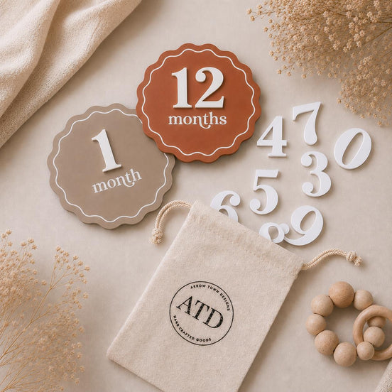 Scalloped baby milestone discs showing 1 and 12 months, with interchangeable white numbers and a storage pouch.