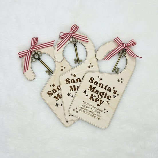 Three engraved wooden Santa's Magic Key door hangers with keys and red-and-white striped bows.
