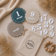 Blue and neutral scalloped baby milestone discs with white month numbers and a drawstring storage pouch.