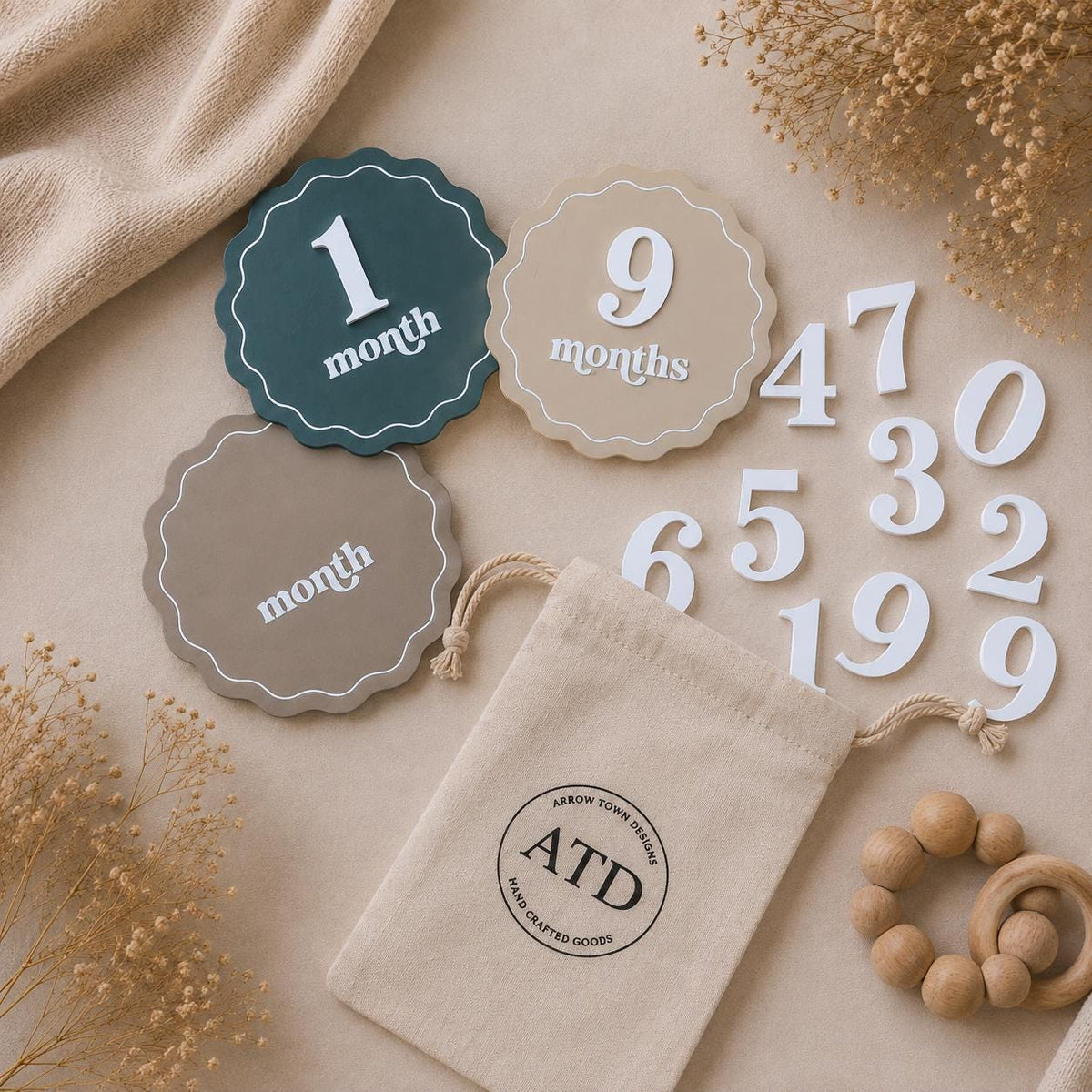 Blue and neutral scalloped baby milestone discs with white month numbers and a drawstring storage pouch.