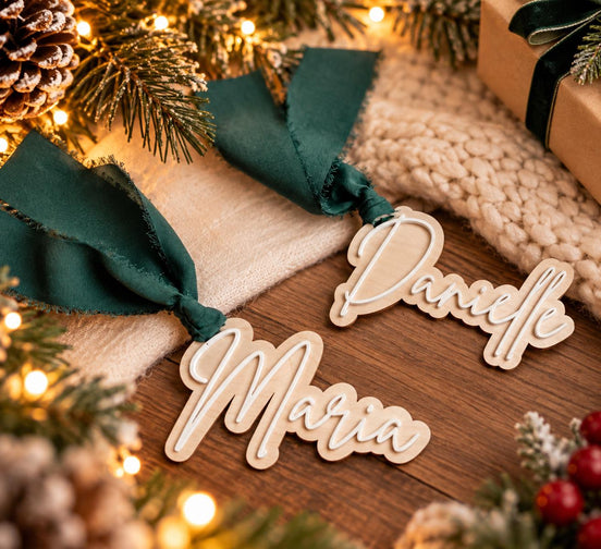 Danielle and Maria layered wooden script tags with green ribbons beside warm Christmas lights.
