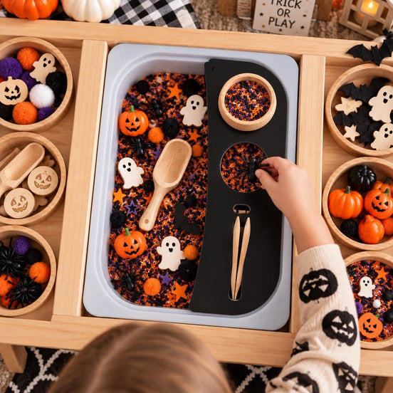 Child using a black sensory-bin organizer with bowl and scoop slots in a Halloween play setup.